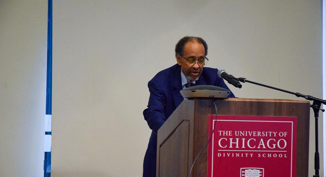 Michael Dawson, a Black man in a suit, standing in front of a UChicago podium speaking